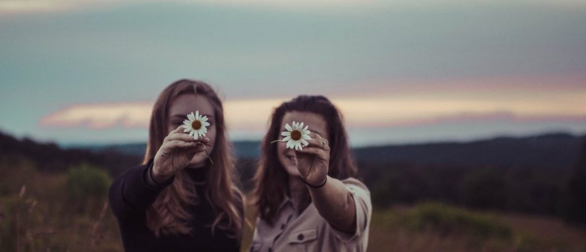 two young women with flowers in front of their face; metaphor for understanding Instagram benchmarks and easy goal setting
